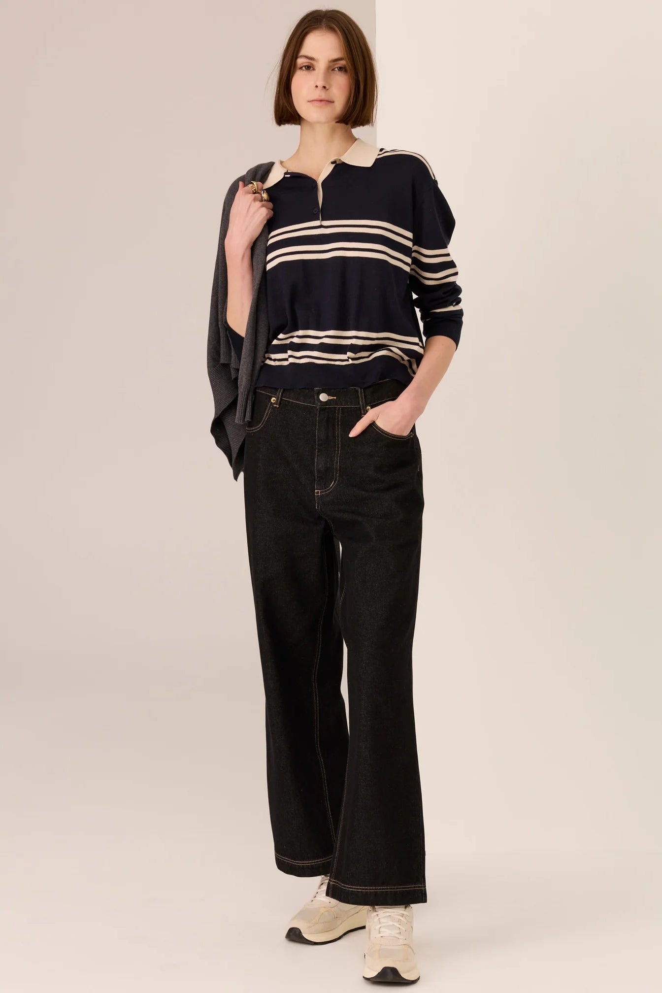 Person wearing a striped polo long sleeve sweater and black pants on a plain background