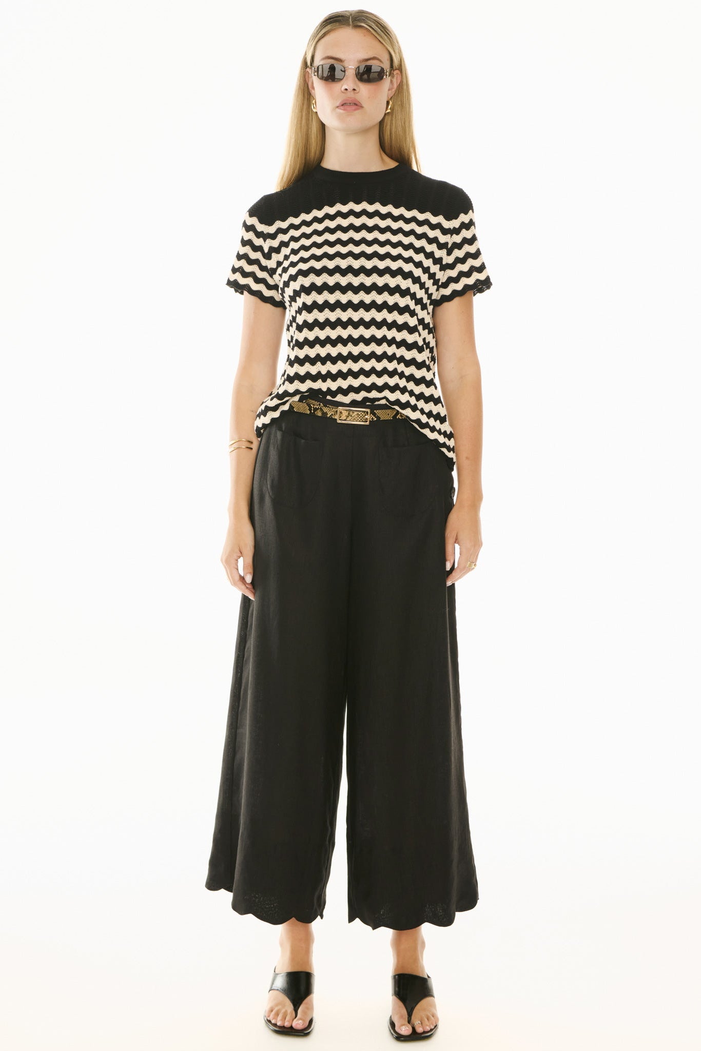 Woman wearing black and white knit short sleeve top and black pants on white background. 