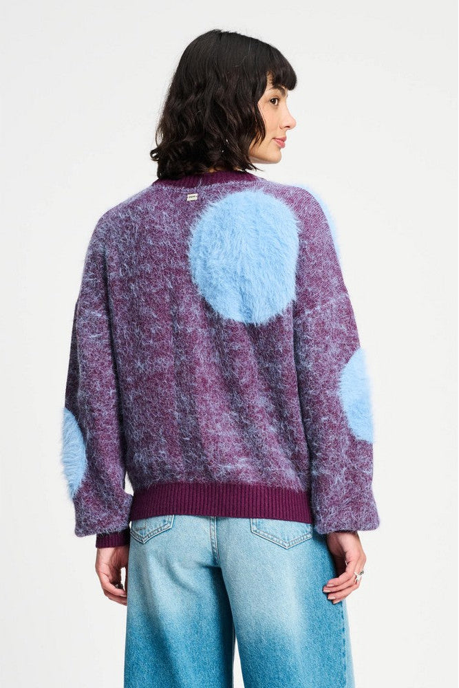 Person wearing a purple sweater with blue circular patterns on a white background