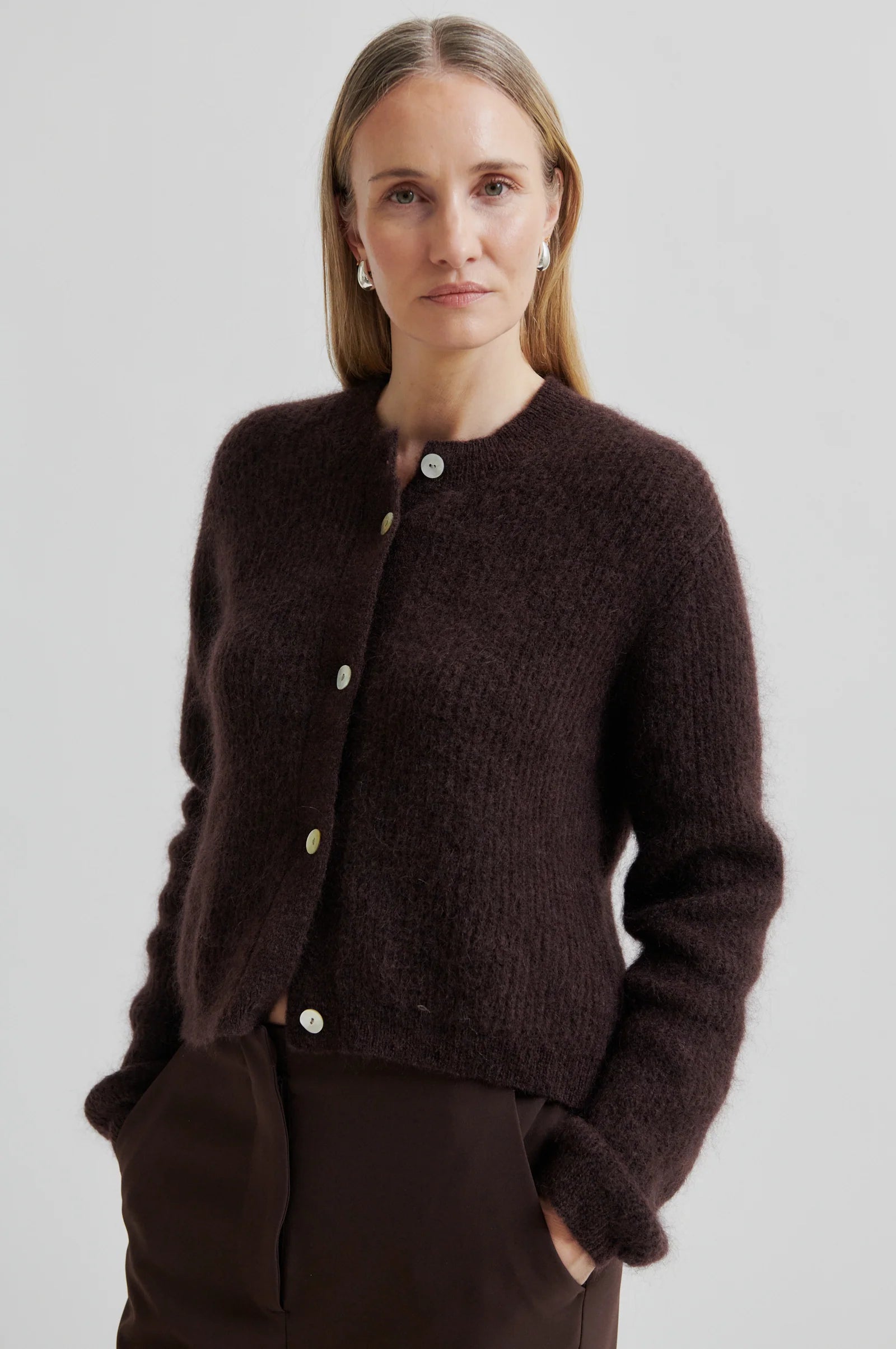 Woman wearing a dark brown cardigan with buttons on a plain background