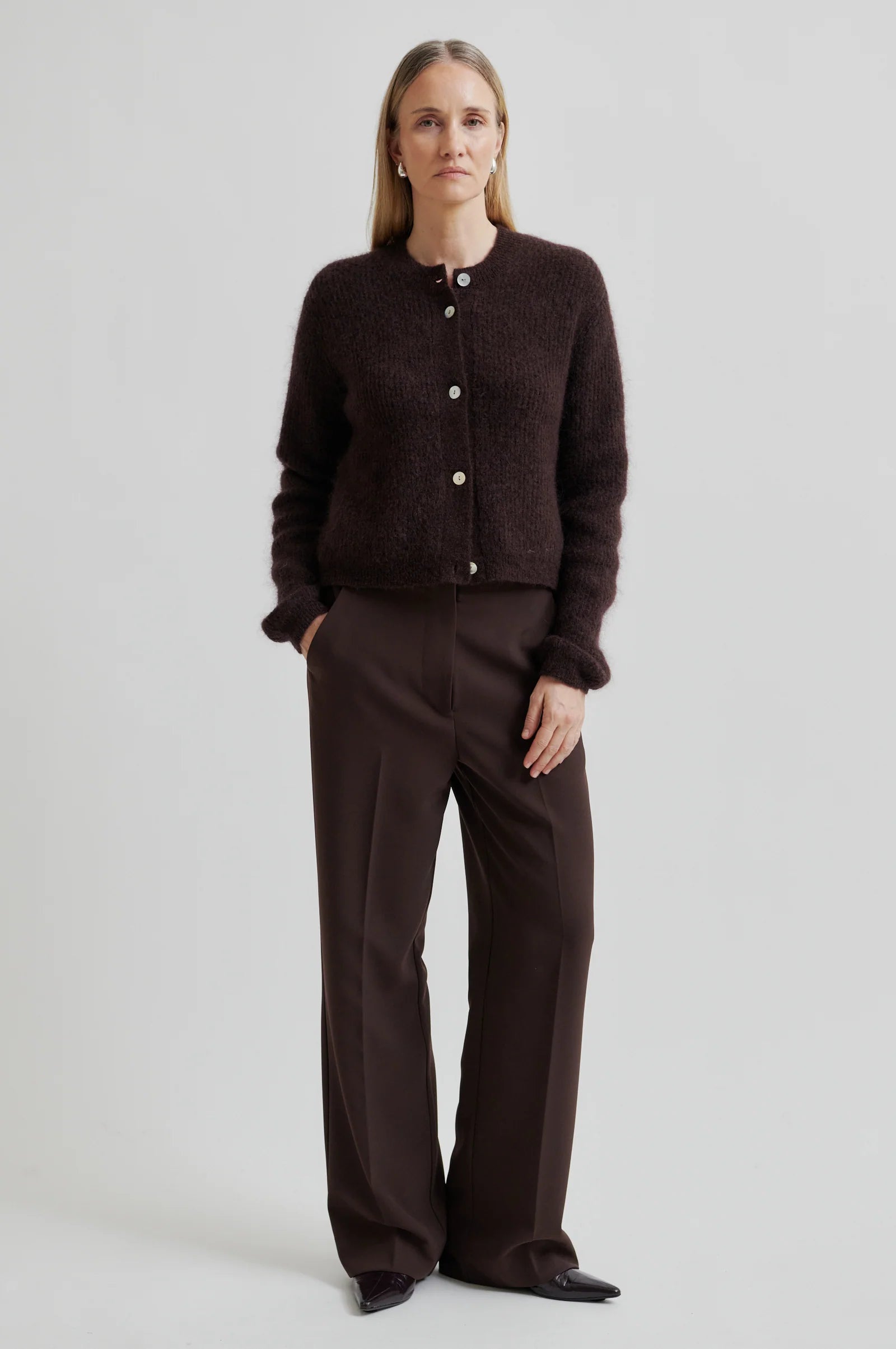 Woman wearing a brown cardigan and pants on a light gray background