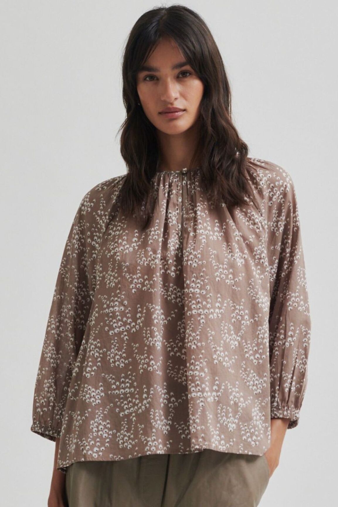 Woman wearing a brown floral blouse against a plain background