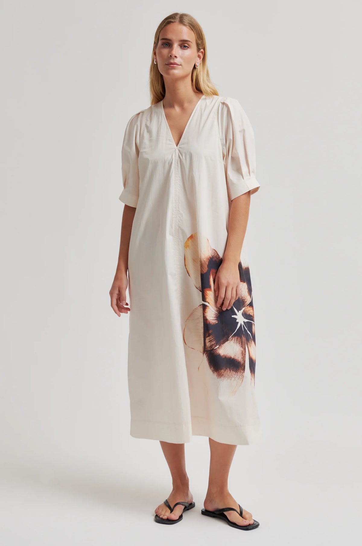 Model wearing a cream dress with puff sleeves and an abstract floral design on bottom left a plain background