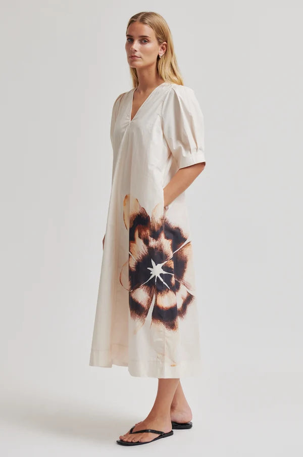 Model wearing a cream dress with puff sleeves and an abstract floral design on bottom left a plain background