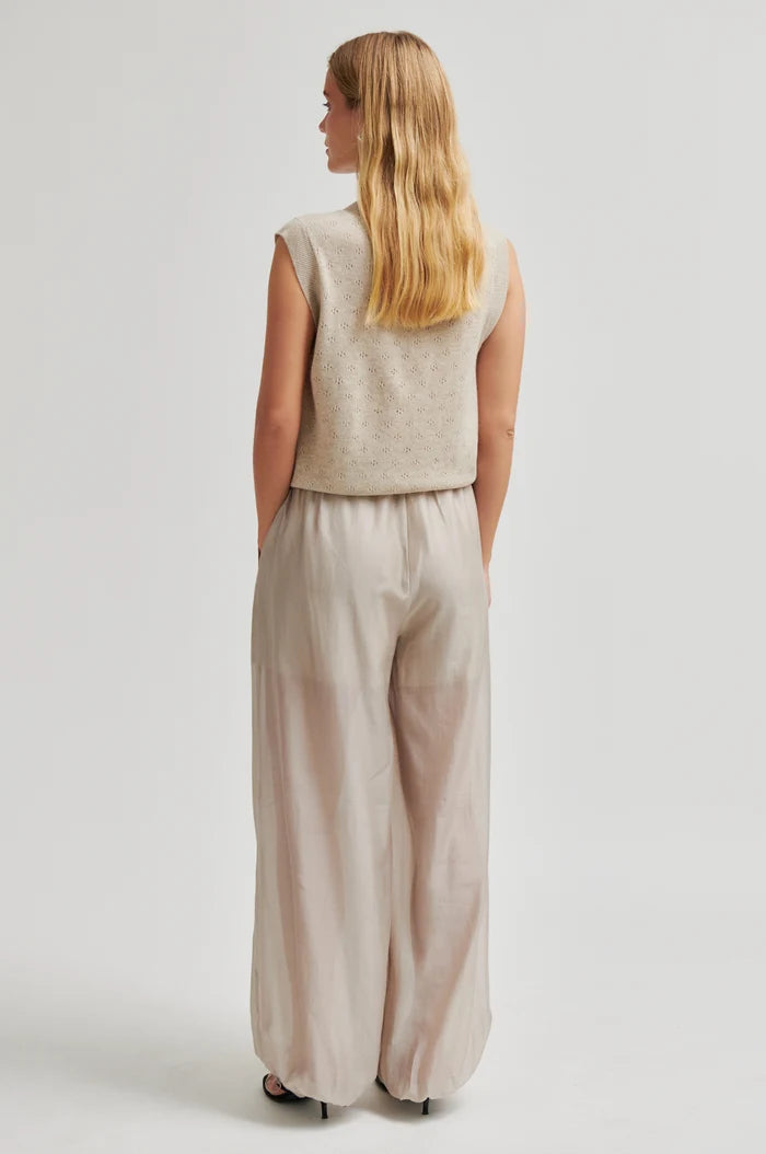 Woman shown from the back wearing a beige sleeveless top and wide-leg pants on a light grey background