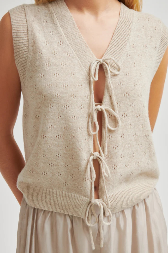 Woman shown up close wearing a beige knitted vest with lace-up back on a plain background