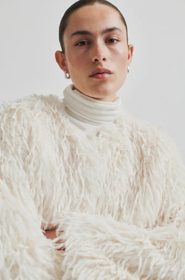 Model wearing Shaggy cream jacket with long sleeve cropped. Paired with cream turtle neck top and cream pants. 