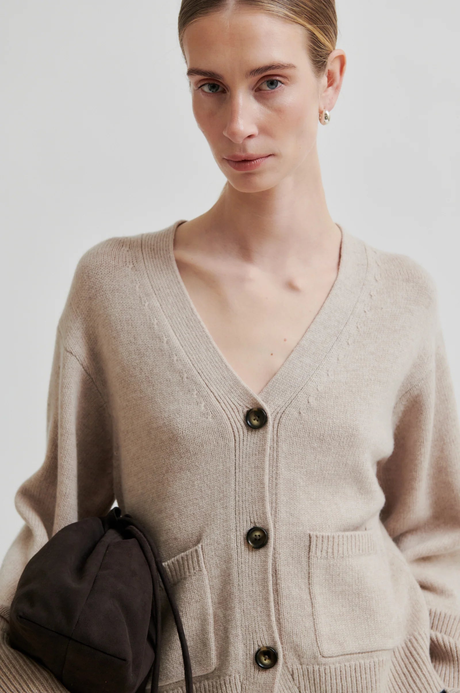 Woman wearing a beige cardigan with a plain background