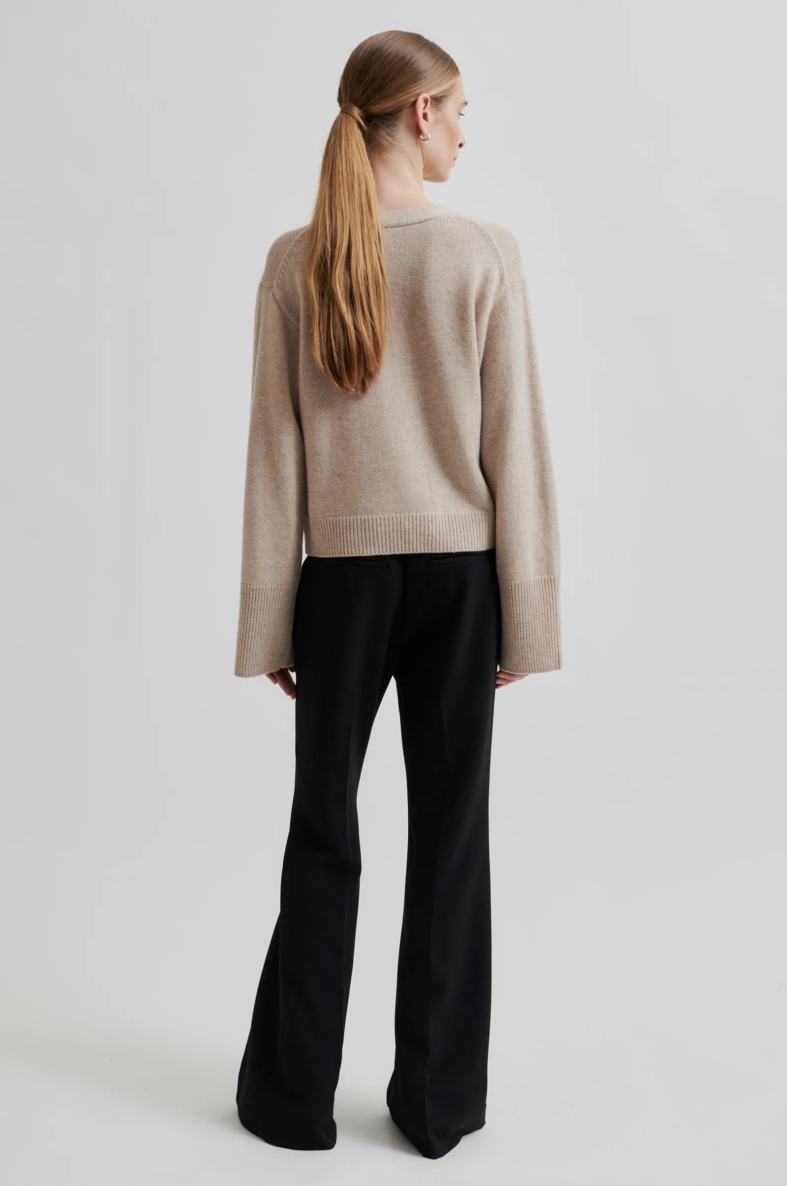 Person wearing a beige sweater and black pants on a light gray background