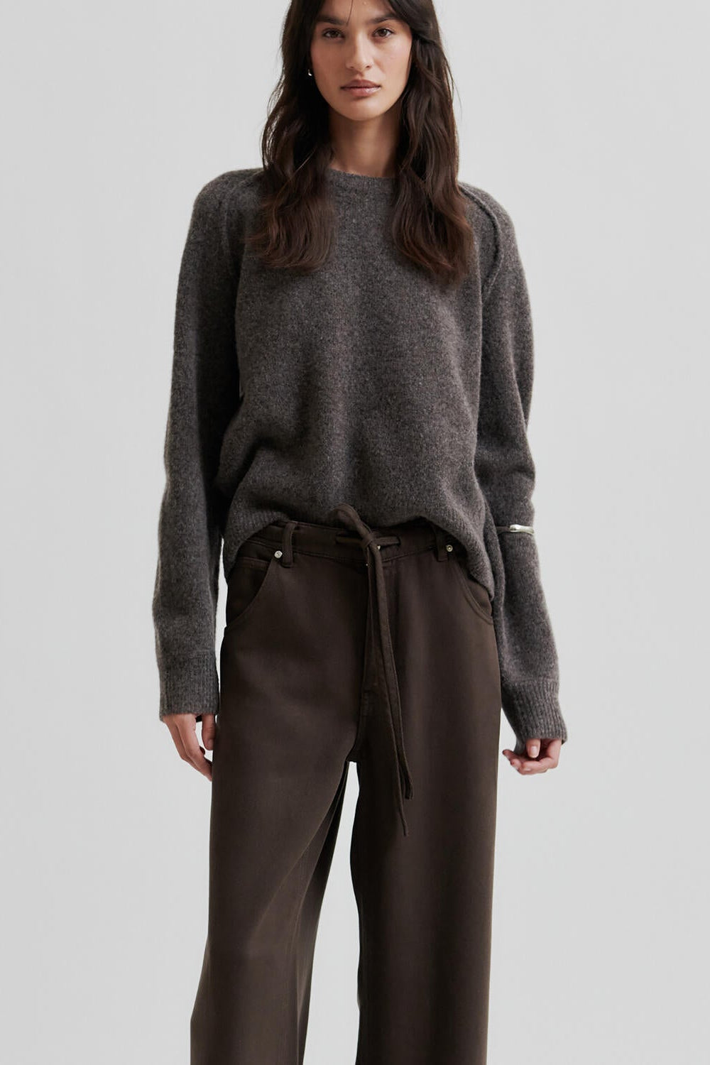 Woman wearing a brown sweater and brown pants on a light gray background