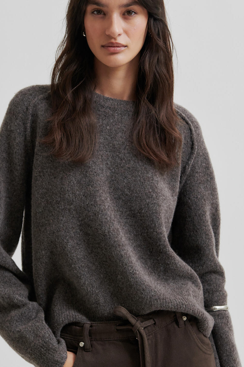 Woman wearing a brown sweater and brown pants on a light gray background