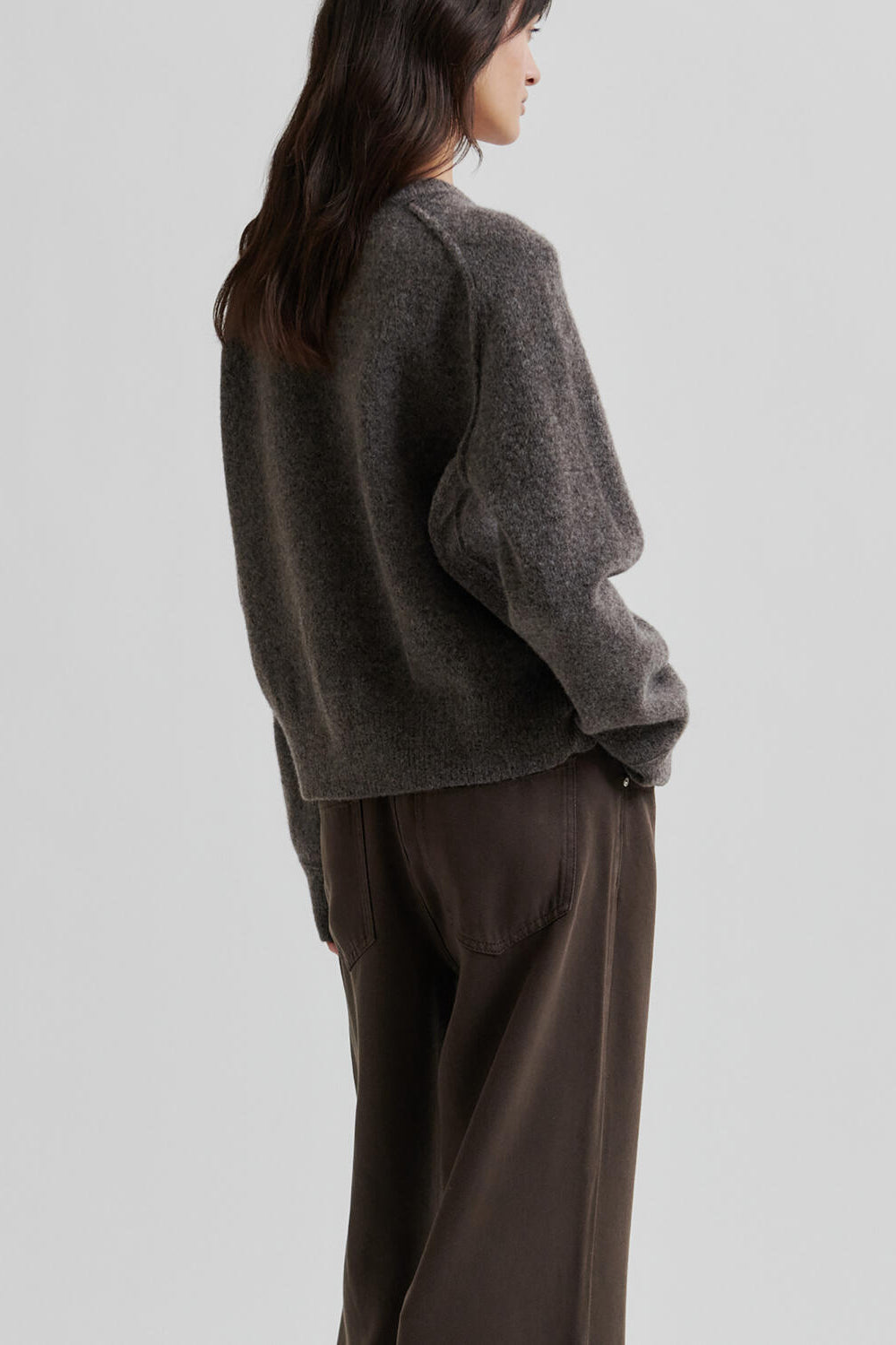 Woman wearing a brown sweater and brown pants on a light grey background