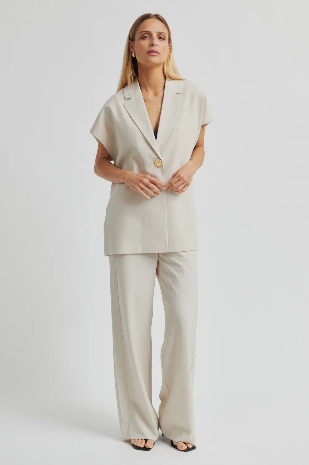 Woman wearing a beige outfit with wide-leg pants on a white background