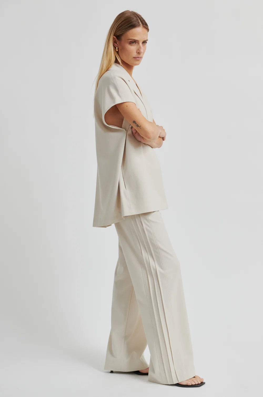 Woman wearing a beige outfit with wide-leg pants on a white background