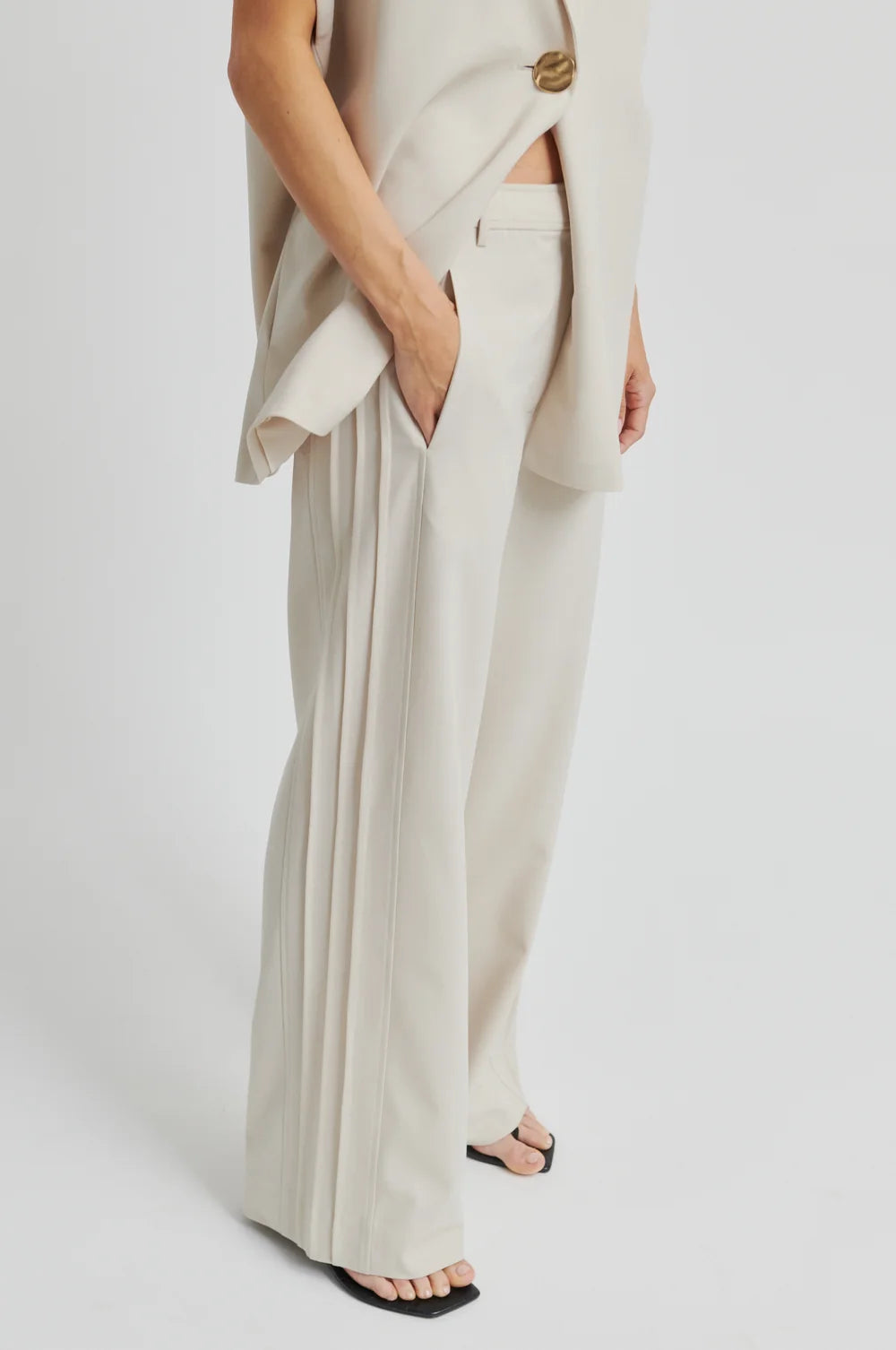 Woman wearing a beige outfit with wide-leg pants on a white background