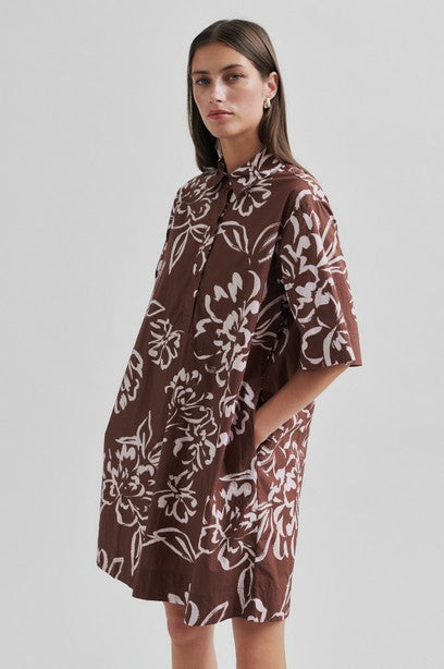 Woman wearing a brown floral tunic dress with collar on a white background