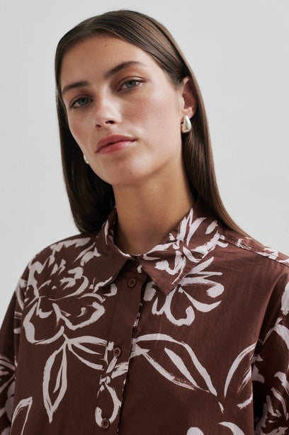 Woman wearing a brown floral tunic dress with collar on a white background