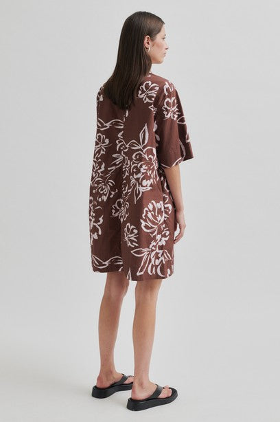 Woman wearing a brown floral tunic dress with collar on a white background