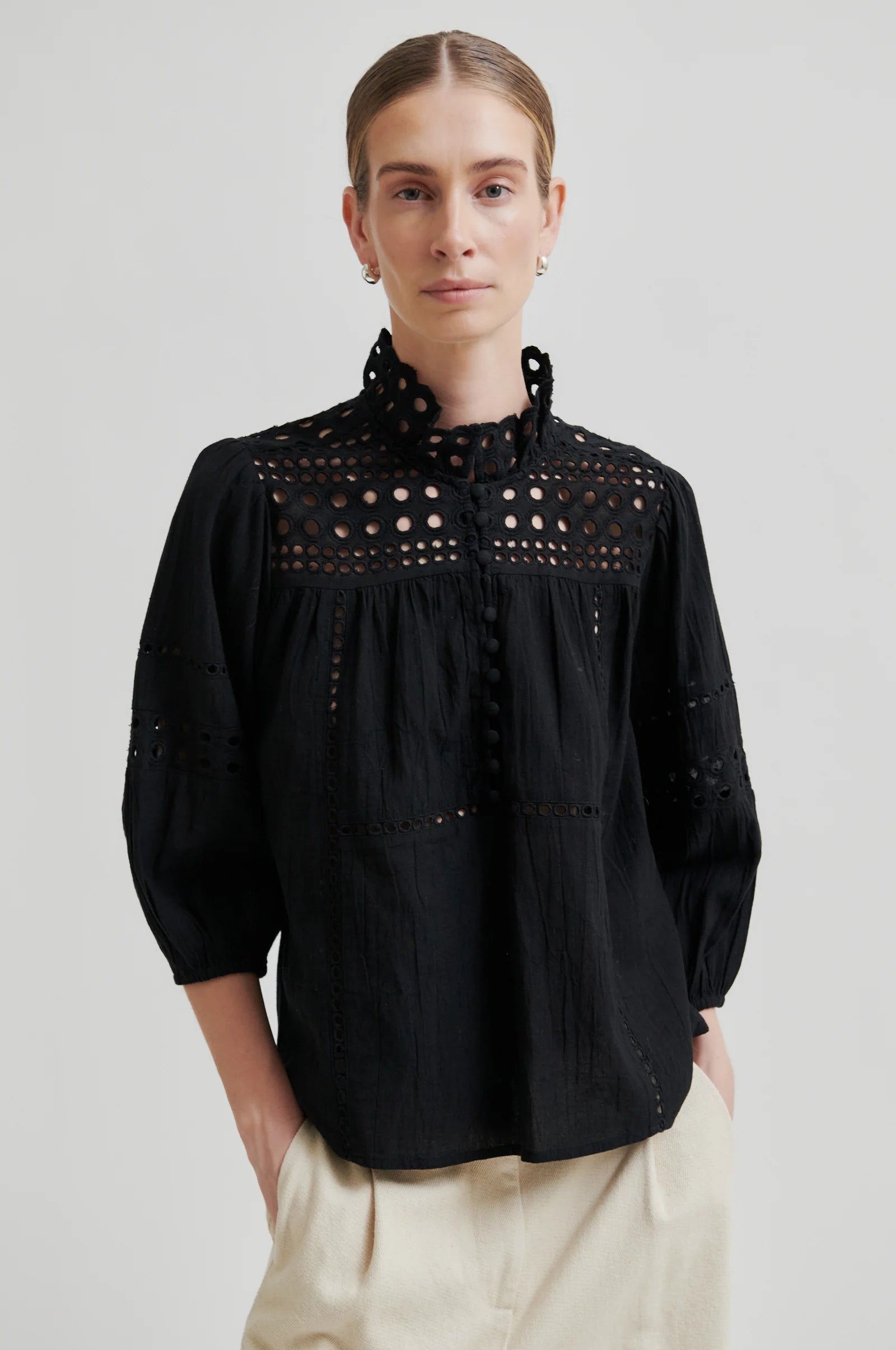 Woman wearing a black blouse with intricate detailing on a plain background