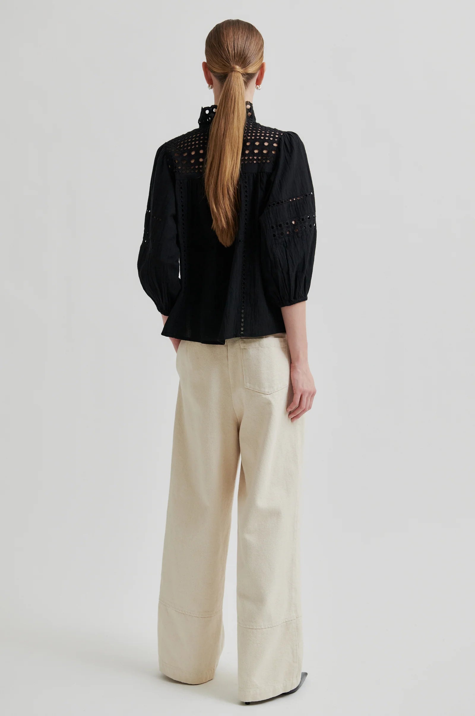 Person wearing a black jacket with studs and beige pants on a light gray background