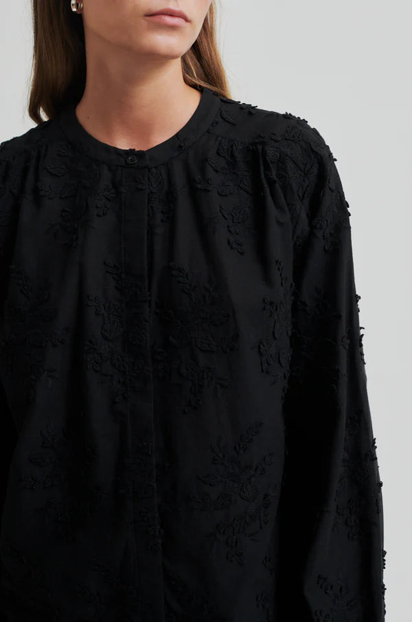 Model wearing a black oversized shirt with embroidery close up to show detail.