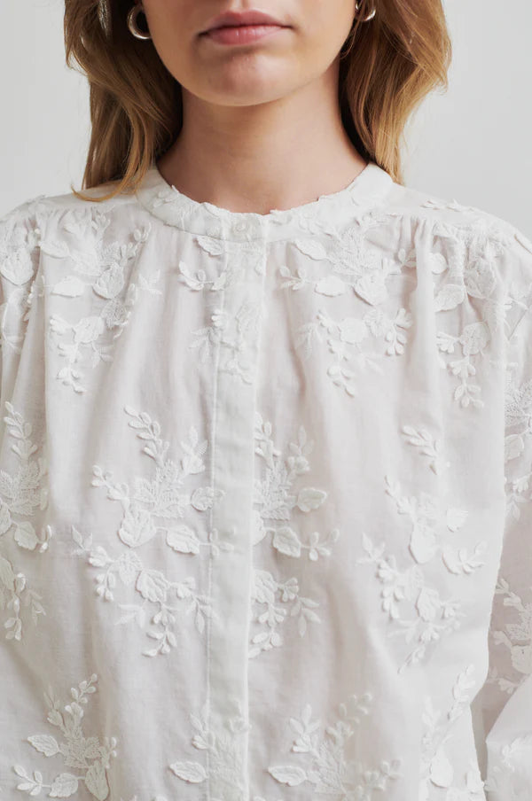 embroidered white shirt with long sleeve paired with neutral wide leg pants. 