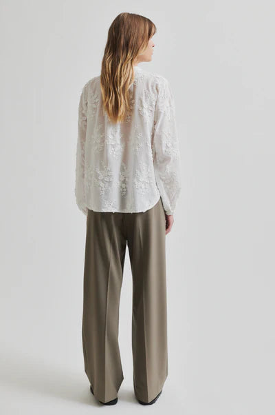 model wearing collarless embroidered white shirt with long sleeve paired with neutral wide leg pants. 