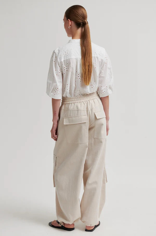 Woman shown from the back wearing a short sleeve white blouse and beige pants on a plain background