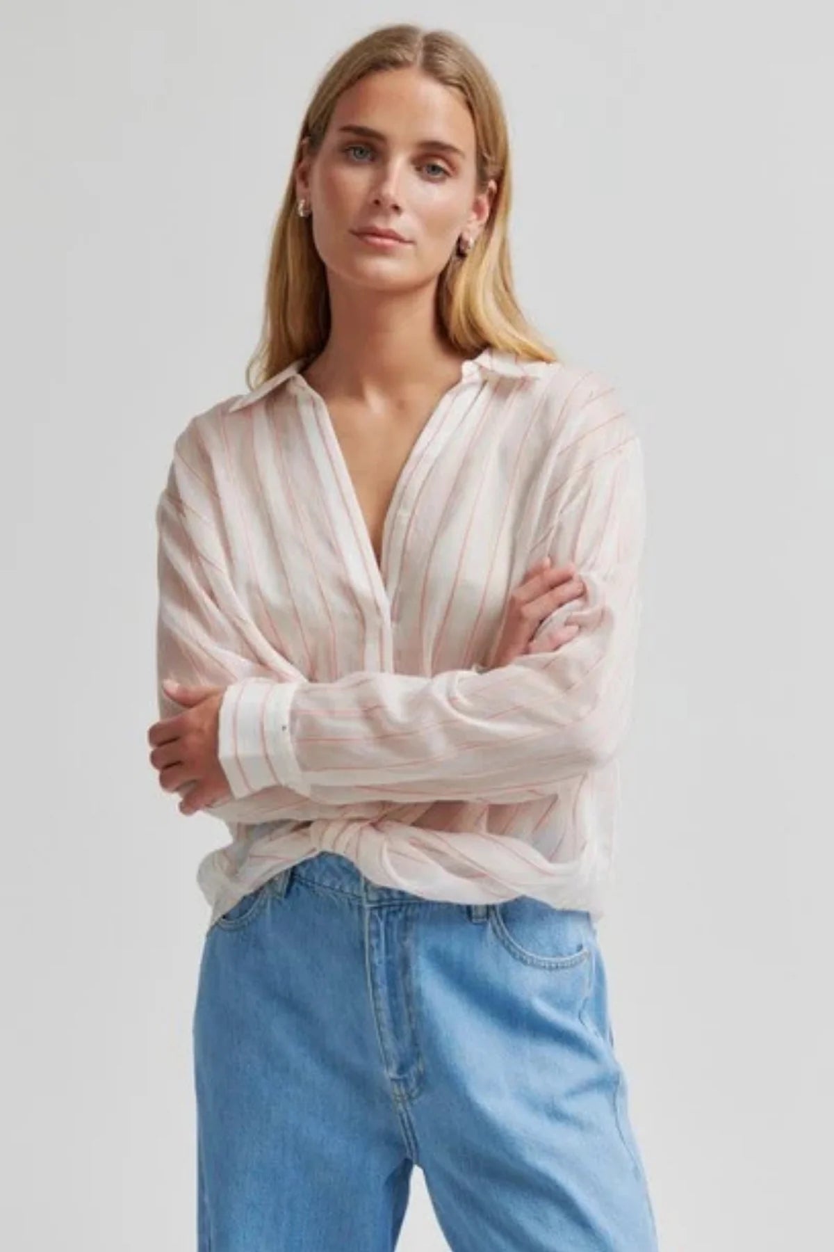 Woman wearing a coloured striped sheer shirt and blue jeans against a plain background