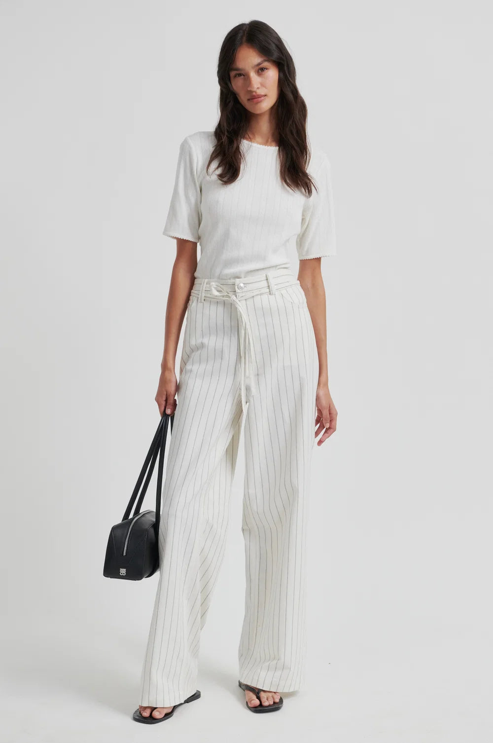 Woman wearing a white top and striped pants holding a black handbag on a white background