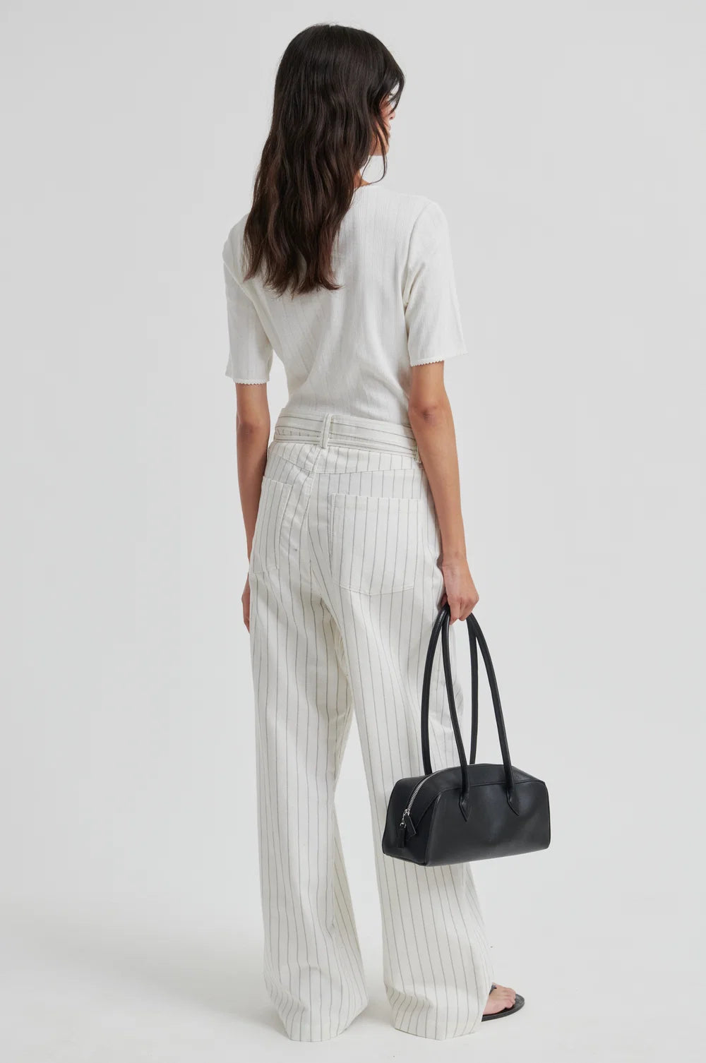 Woman in white outfit holding a black handbag on a plain background