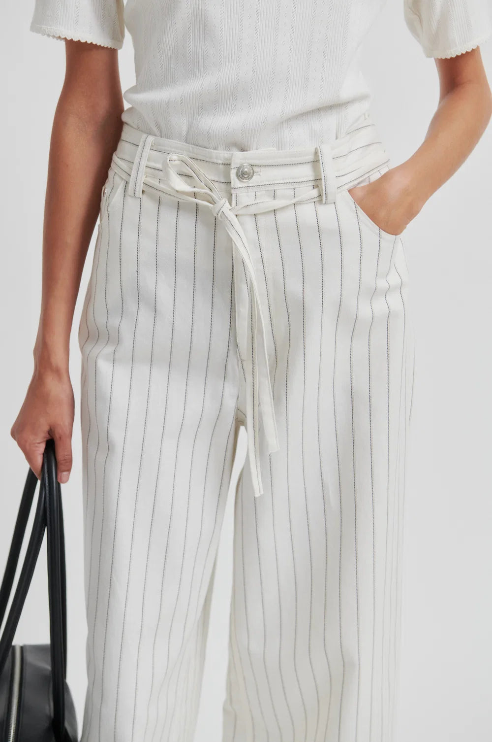 Person wearing a white top and pinstripe white denim jean pants with a black handbag.