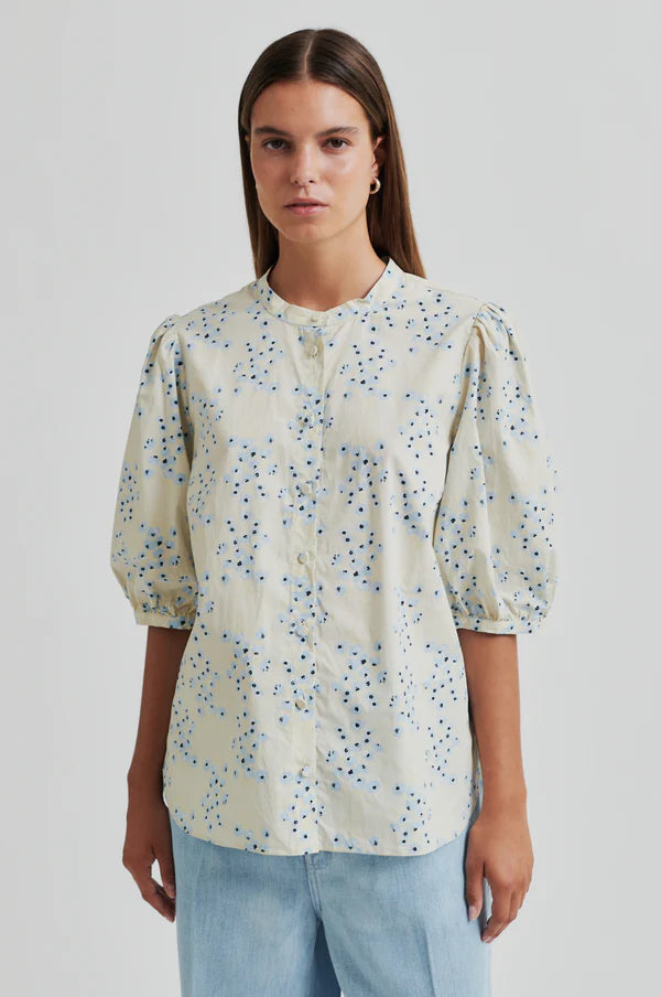 Model wearing a blue floral print blouse on a cream base with puffed sleeves. 