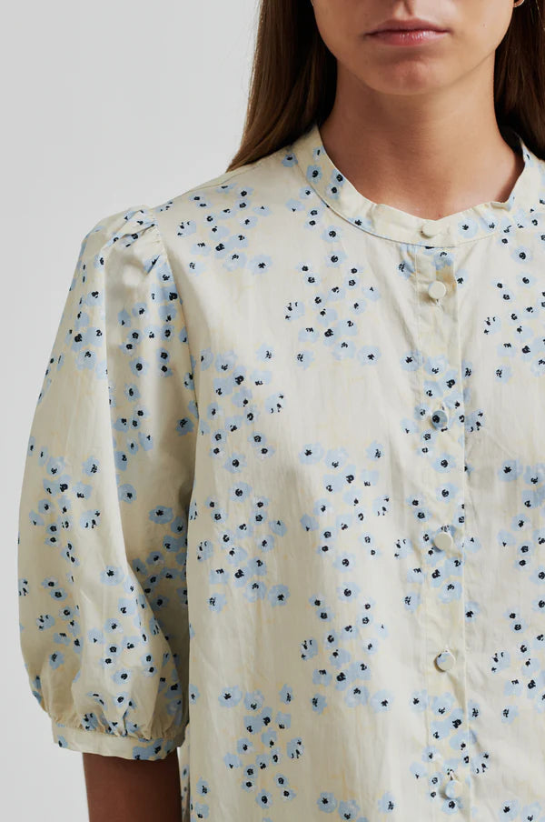 Model wearing a blue floral print blouse on a cream base with puffed sleeves.