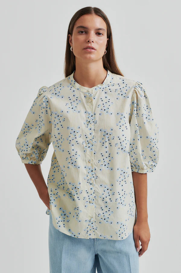 Model wearing a blue floral print blouse on a cream base with puffed sleeves.