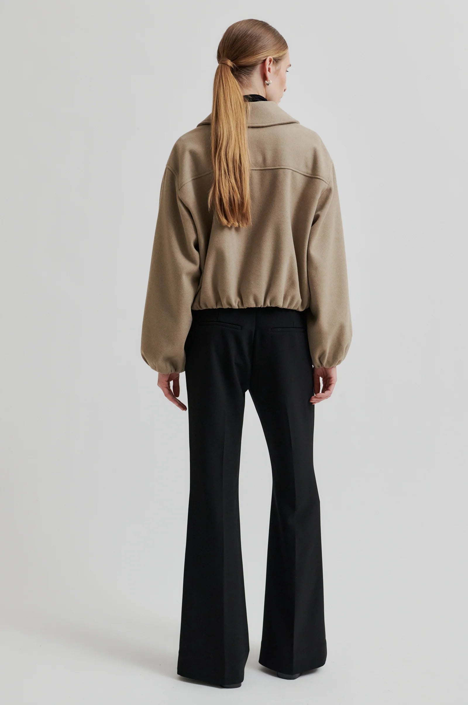 Person wearing a beige jacket and black pants on a light gray background