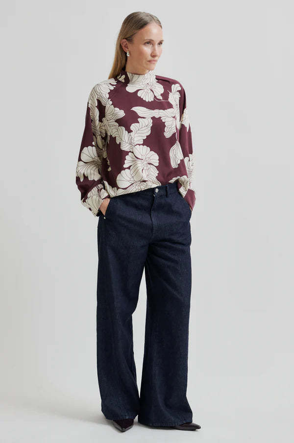 Woman wearing a burgundy floral blouse and dark pants on a light gray background