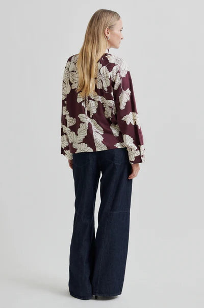 Woman wearing a patterned blouse and dark pants on a white background