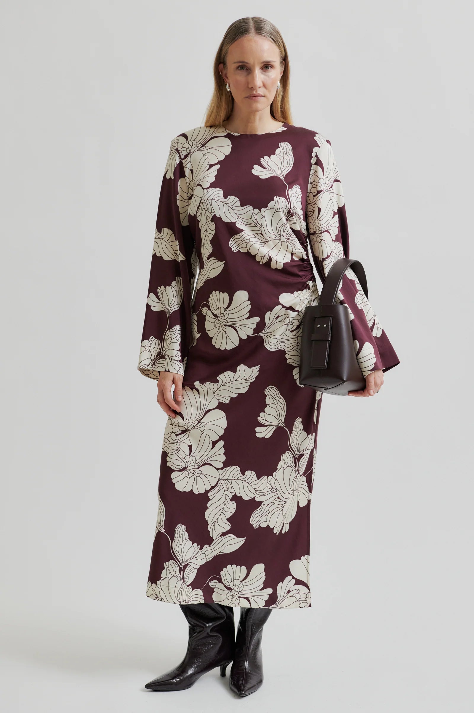 Woman wearing a long sleeve burgundy  maxi dress with white floral print with a plain background