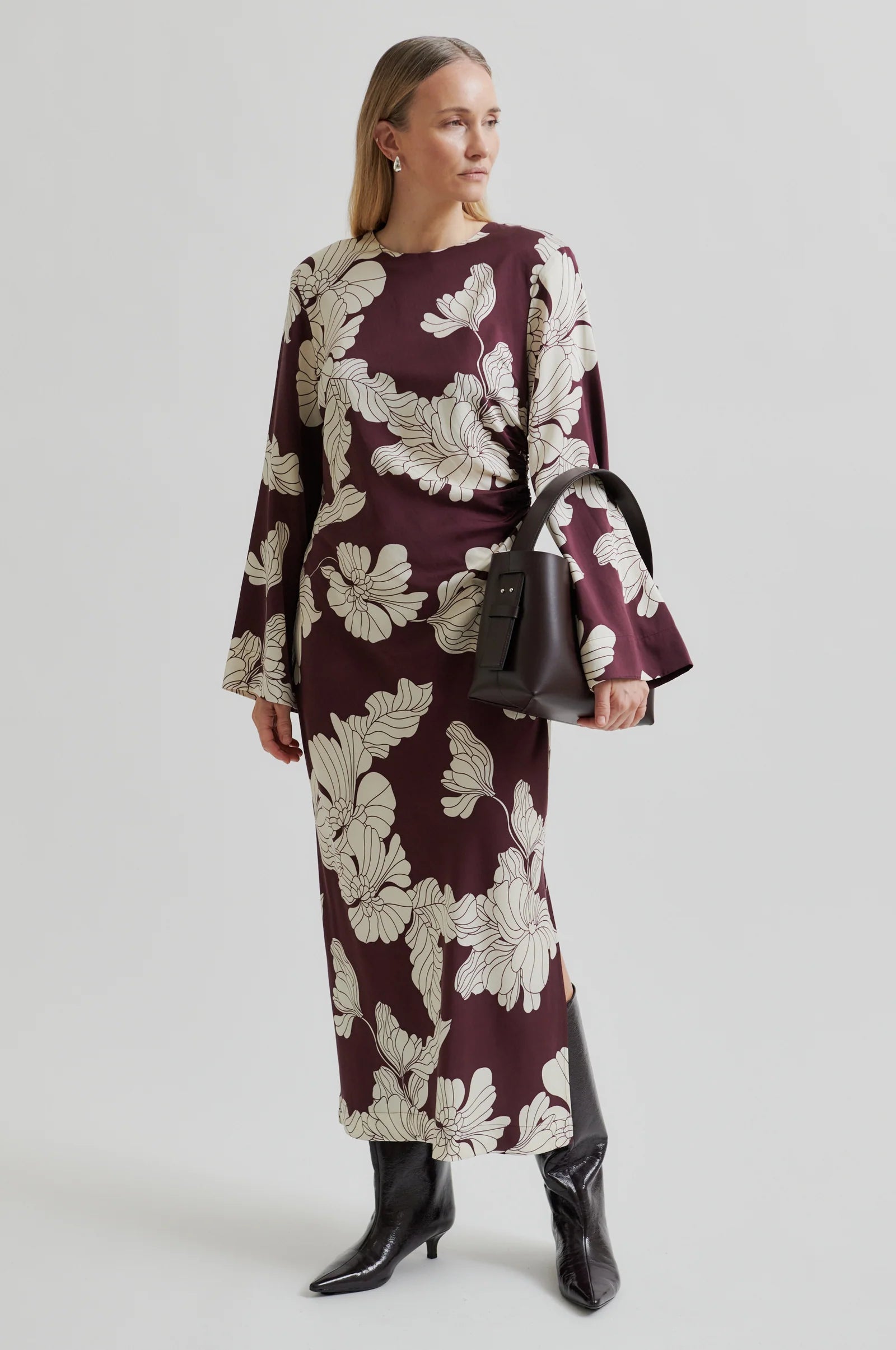 Woman wearing a long sleeve burgundy  maxi dress with white floral print with a plain background