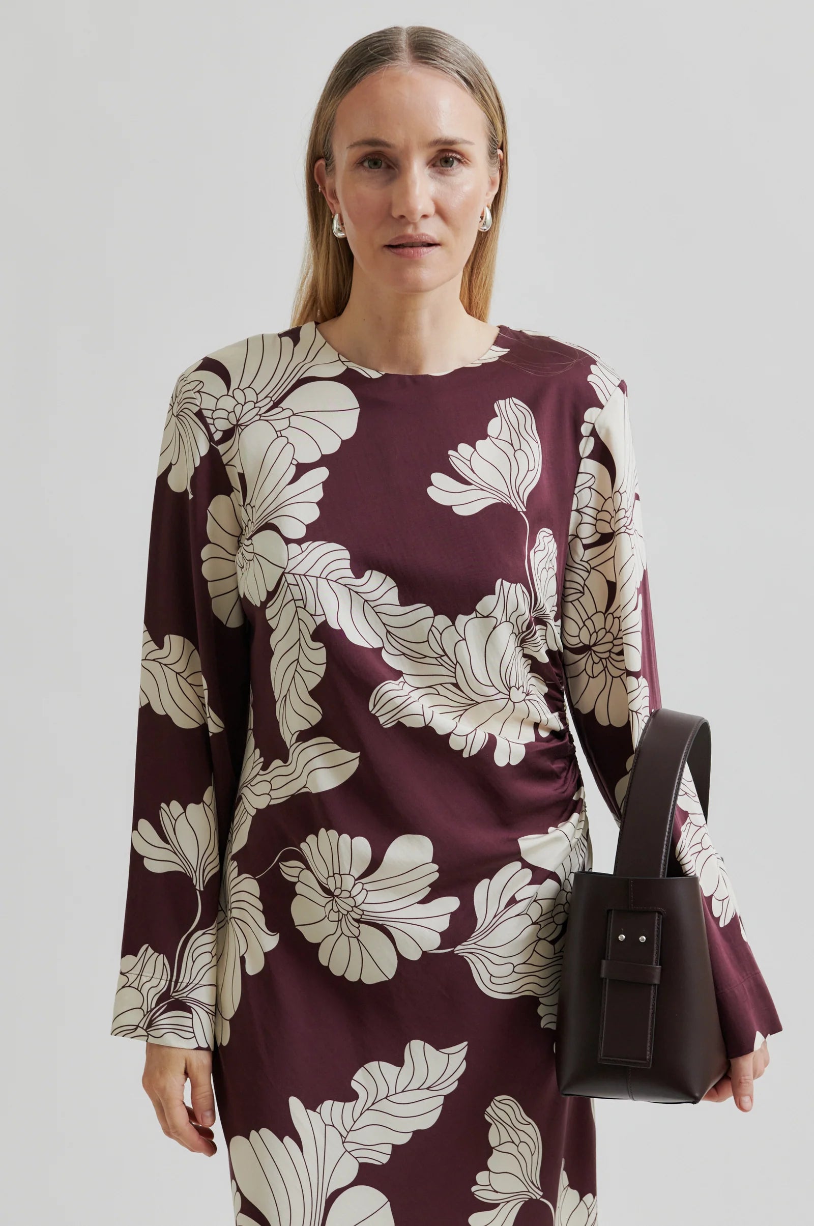 Woman up close wearing a long sleeve burgundy  maxi dress with white floral print with a plain background