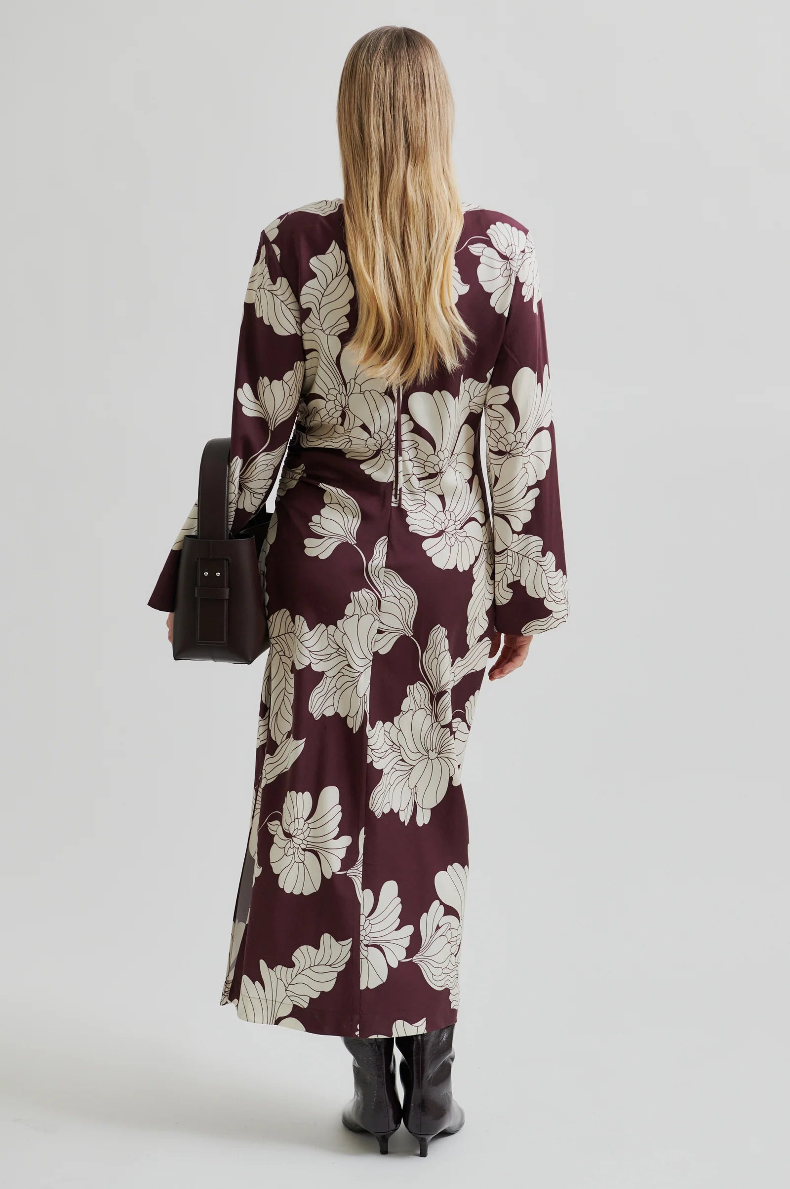 Woman wearing a long sleeve burgundy  maxi dress with white floral print with a plain background