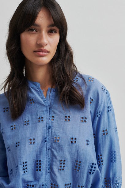 Model wearing blue broderie short sleeve shirt with tan shorts on a light background. 