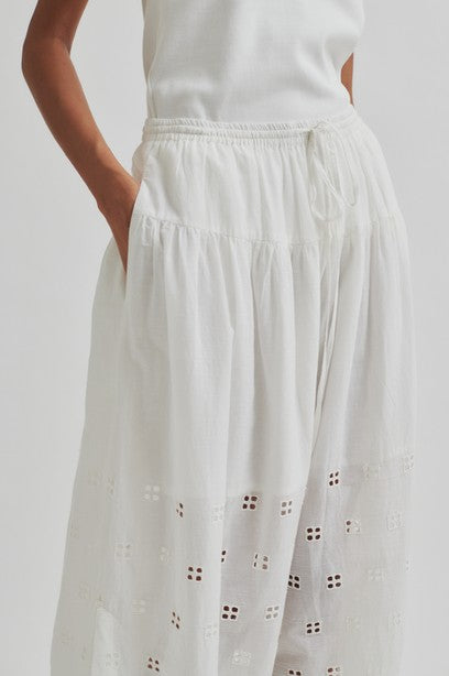 Woman wearing a white sleeveless top and white skirt with cut-out details on a plain background