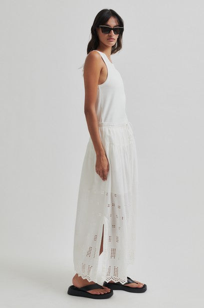 Woman wearing a white sleeveless top and white skirt with cut-out details on a plain background