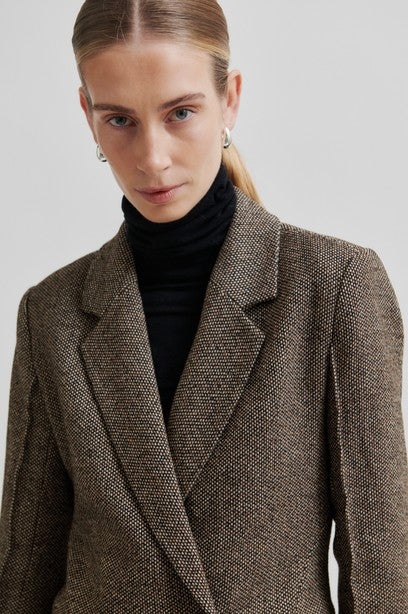 Woman wearing a brown blazer over a black turtleneck on a plain background