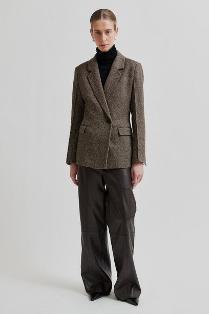 Person wearing a brown blazer and black pants on a light gray background