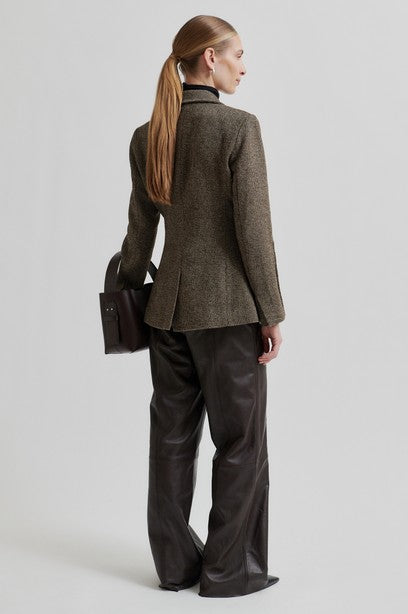 Person wearing a brown blazer and black leather pants on a light gray background