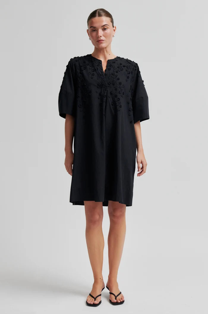 Woman wearing a black midi dress with floral embroidery on a white background