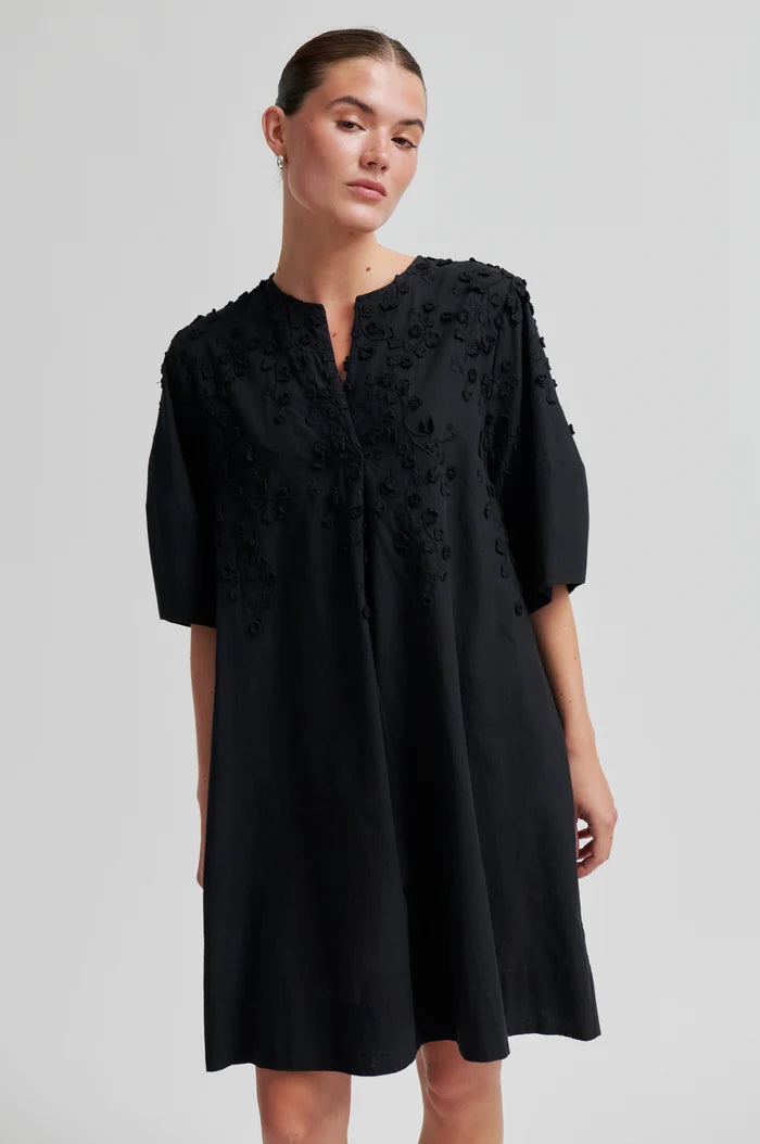 Woman wearing a black midi dress with floral lace details on a light grey background